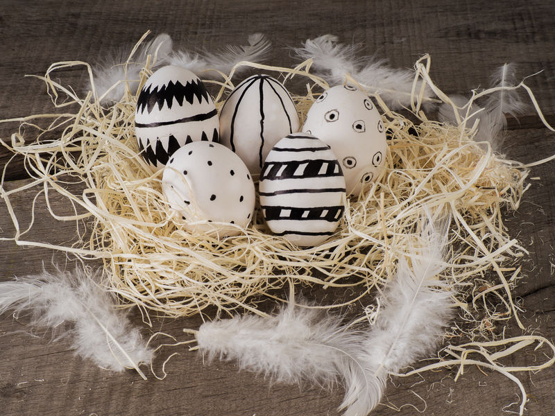 在一张有白色羽毛的木桌上放一些手绘复活节彩蛋