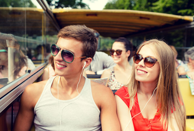 友谊旅行度假夏天和人的概念-带耳机的微笑情侣乘坐旅游巴士旅行