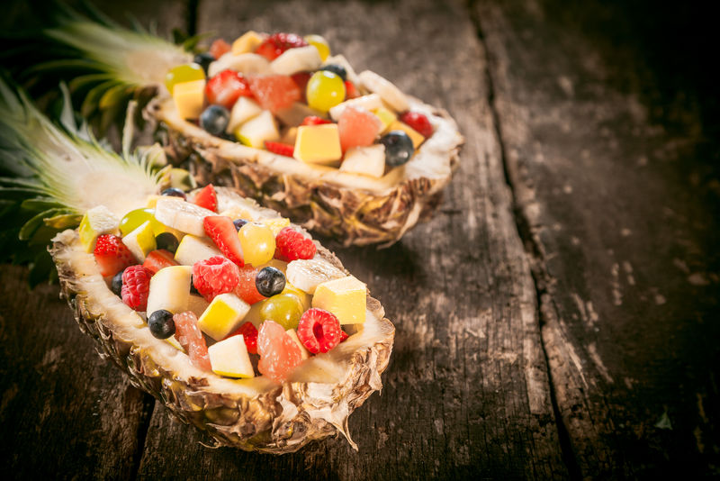 把新鲜的热带水果沙拉放在菠萝船上的乡村木桌上