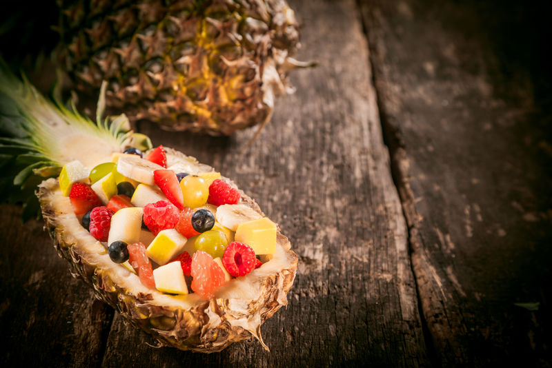美味可口的新鲜水果沙拉放在菠萝船上的木桌上近距离拍摄