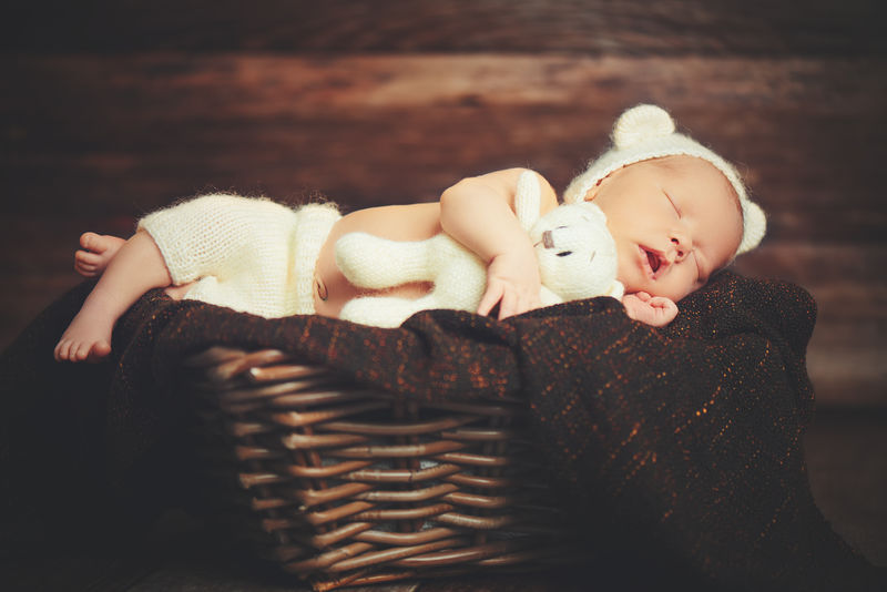可爱的新生儿在熊帽子睡在篮子玩具泰迪是