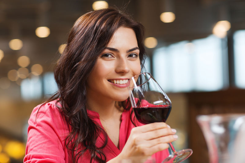 微笑的女人在餐馆里喝红酒