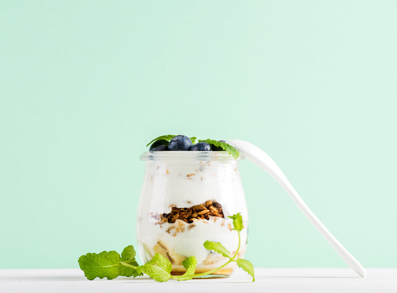 酸奶燕麦格兰诺拉果酱蓝莓和绿叶装在玻璃罐里薄荷味的衬托下