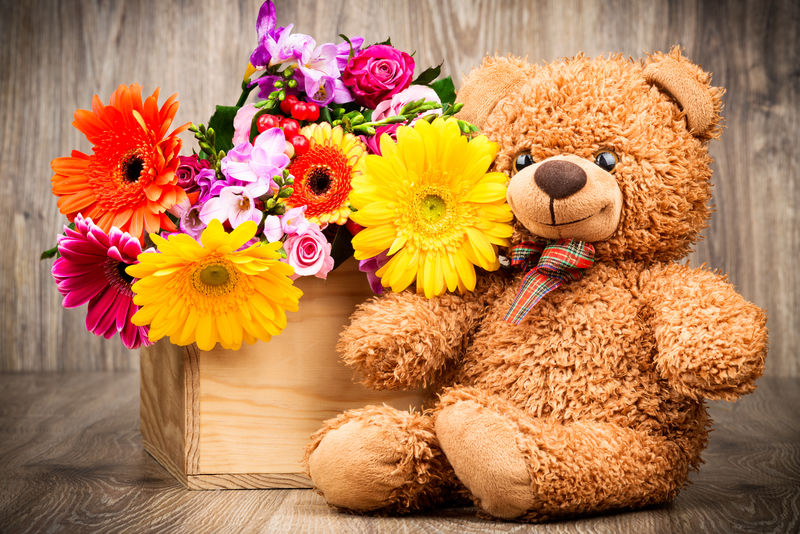 漂亮的花和木制背景的泰迪熊