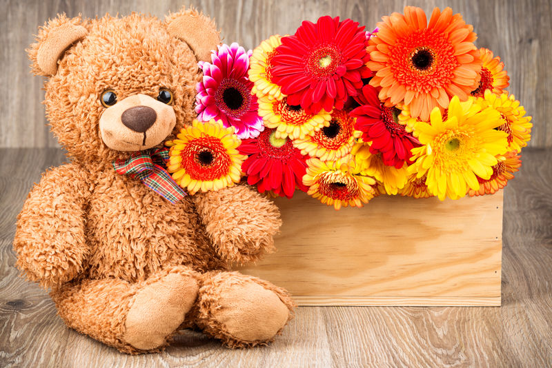 盒子里有漂亮的花和木制背景的泰迪熊