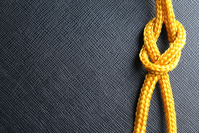 金色绳缆-简单的绳结-特写照片悬挂在黑色人造革背景前