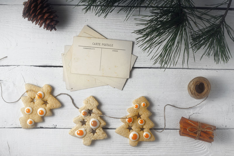 白色木质背景顶视图上的圣诞饼干和明信片花环