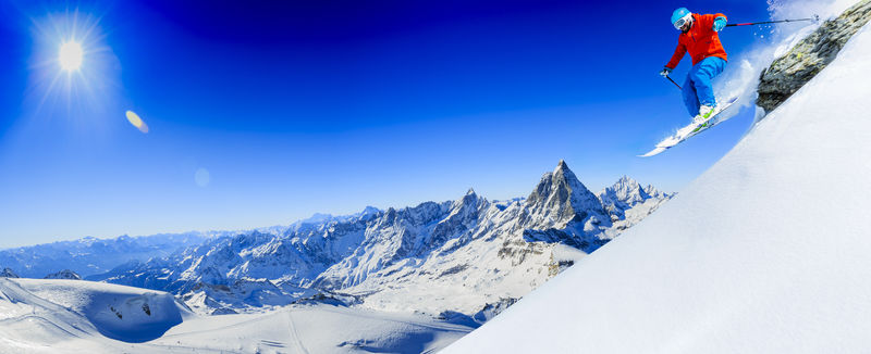 在瑞士阿尔卑斯山的泽马特一名男子从岩石上跳下在背景为马特霍恩的新鲜粉末雪上滑雪