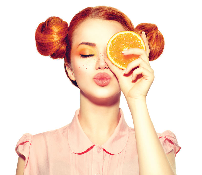 美丽快乐的少女长着雀斑手里拿着多汁的橘子片