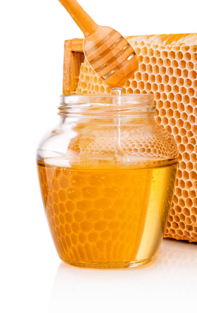 蜂蜜从斗中滴入背景蜂巢上的玻璃罐中