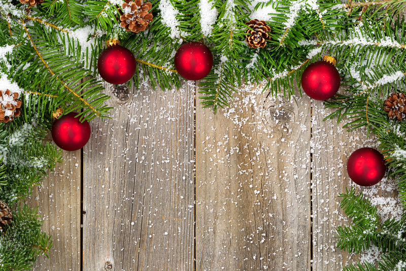雪覆盖着真正的冷杉树枝和圆锥体-红色的装饰物在乡村木板上形成了边界-圣诞节概念