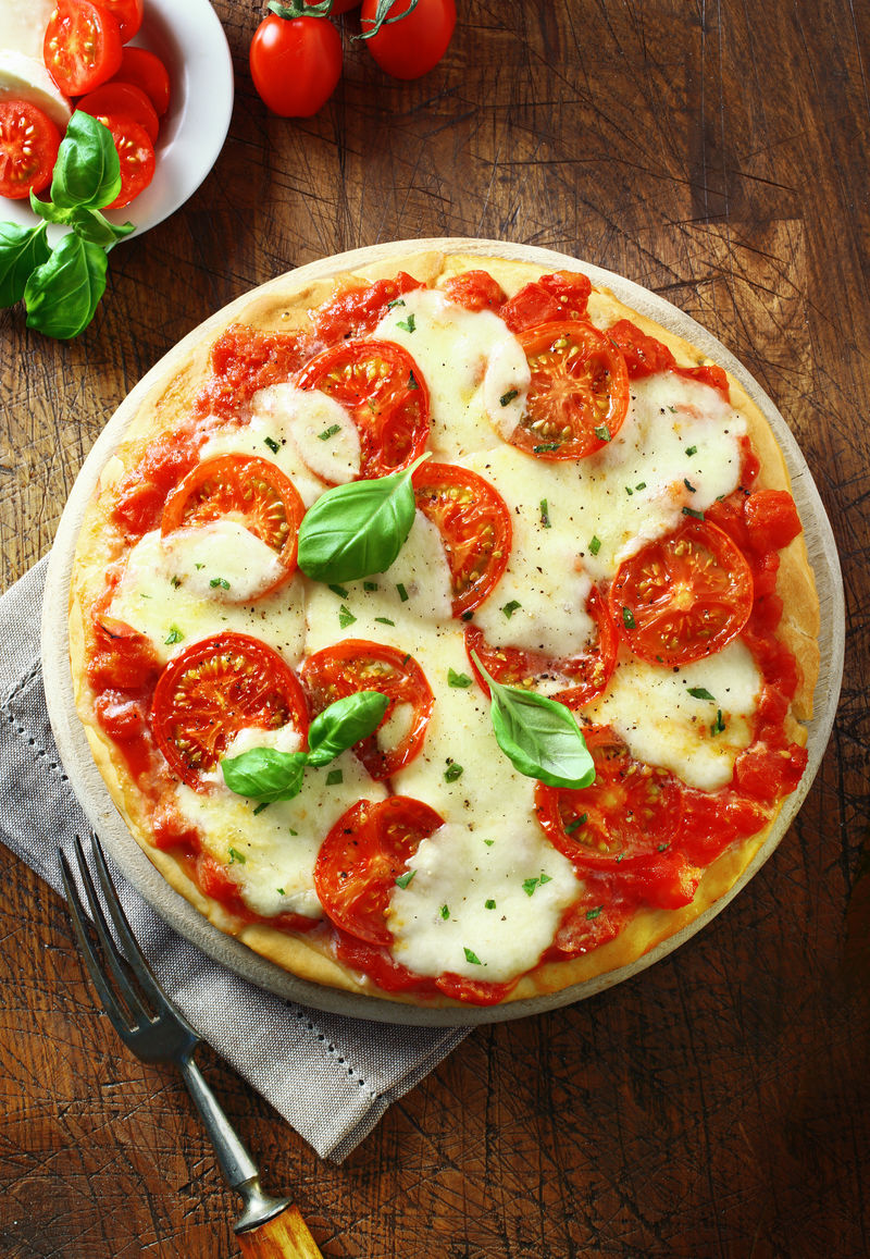 一个色彩鲜艳的新鲜烤番茄和奶酪披萨撒上新鲜香草和罗勒叶放在一张旧木桌上的盘子里