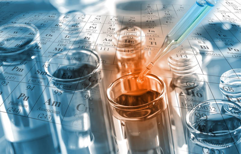 化学家将澄清试剂滴入化学实验室反应测试管中-以周期表为背景