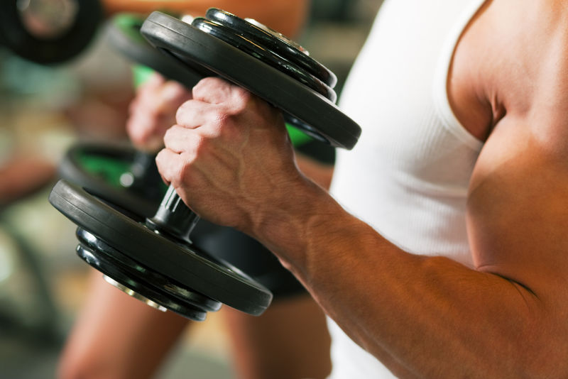 强壮的男人在健身房用哑铃锻炼-背景中女人也举重；注意力集中在手上