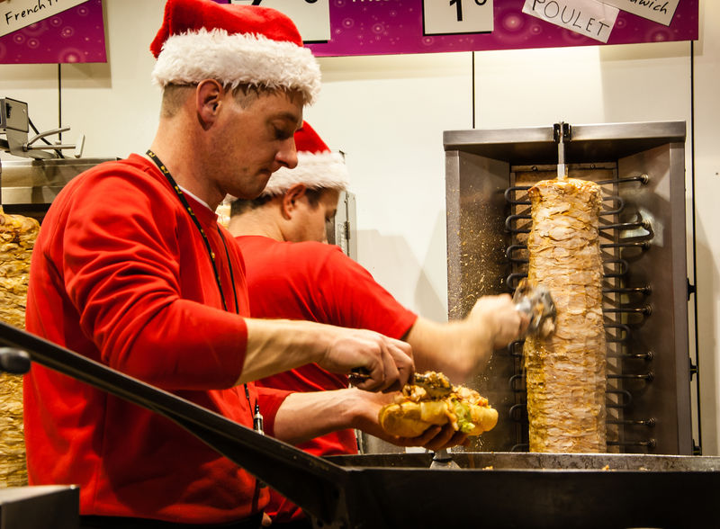 法国巴黎——2013年11月30日：两个戴着圣诞老人帽的身份不明的男人在圣诞市场上做饭和卖烤肉串