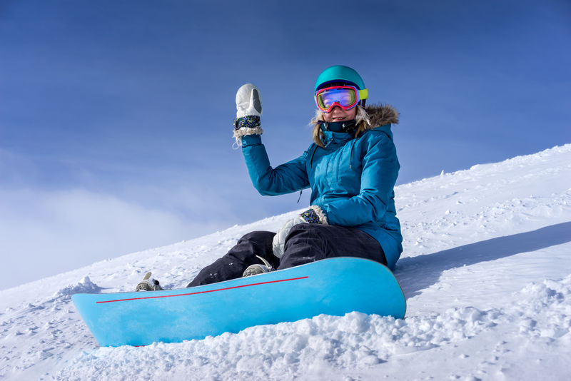快乐的年轻女子滑雪运动员坐在雪坡上-被捆在滑雪场的滑雪板上