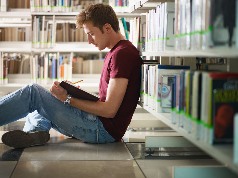 男大学生坐在图书馆的地板上看书-水平形状-侧视图-四分之三长度-复制空间