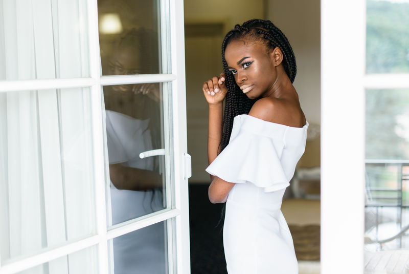 美丽的非洲女孩站在敞开的门前主体在玻璃中反射穿白色连衣裙的女孩