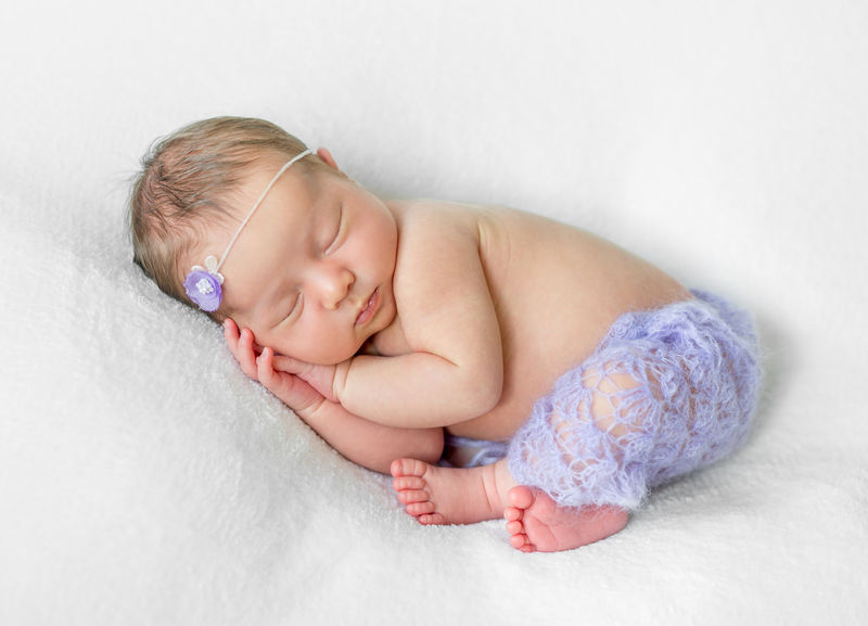 可爱的睡着的新生儿手放在头下穿着紫色内裤