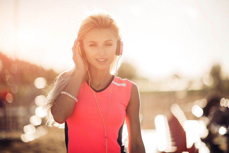 一个运动的少女的肖像她在运动中休息用耳机听音乐在户外微笑健身和运动生活方式阳光明媚