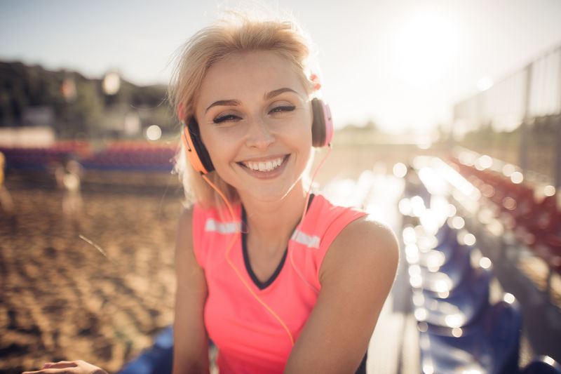 户外运动照片美丽的金发女郎穿着粉红色的彩色西装戴着耳机在海边听音乐