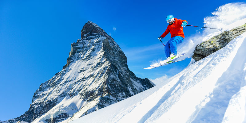 在瑞士阿尔卑斯山的高山上一个阳光明媚的冬日一名男性滑雪者在新鲜的雪中从岩石上跳下滑雪粉雪中的基背景为马特宏峰