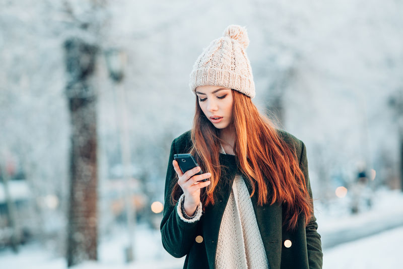年轻女子带着智能手机和冬季景观微笑