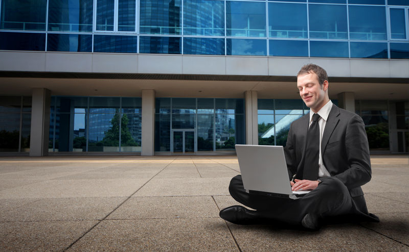 一个商人坐在一栋楼前用笔记本电脑的照片