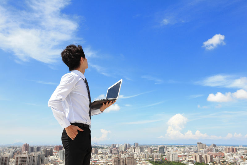 年轻的商业人士使用笔记本电脑-仰望蓝天和云端-背景商业和云计算概念中的城市风光