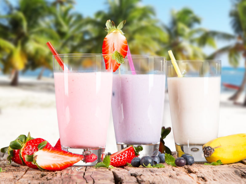 新鲜牛奶草莓蓝莓和香蕉饮料放在木桌上-各种蛋白鸡尾酒配新鲜水果和热带海滩