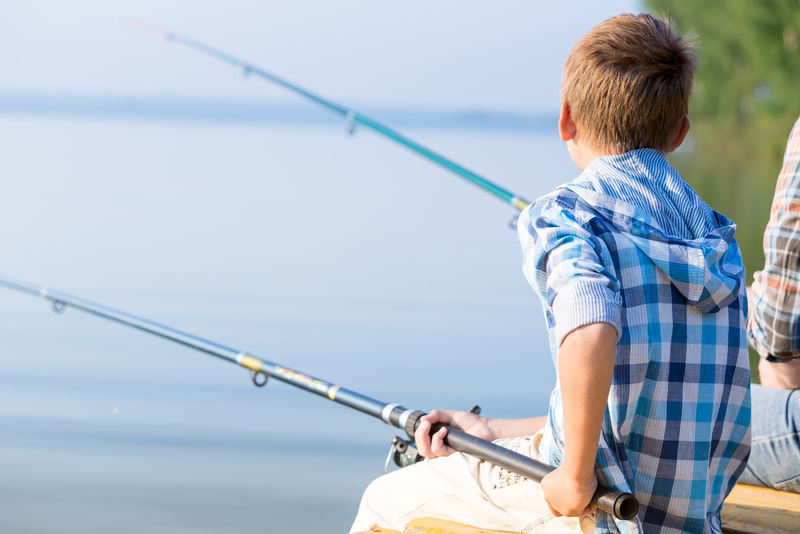 穿蓝衬衫的男孩坐在海边的码头上-手里拿着一根鱼竿