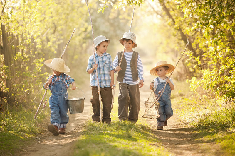 阳光明媚的夏日-四个带着鱼竿的男孩在狭窄的乡间公路上钓鱼