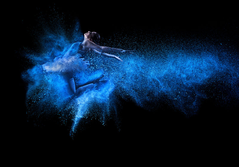 年轻漂亮的舞者跳进蓝色的粉末云中