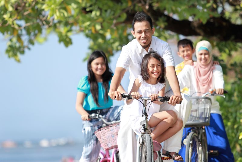 快乐的穆斯林家庭和孩子们喜欢在海滩上骑自行车的照片