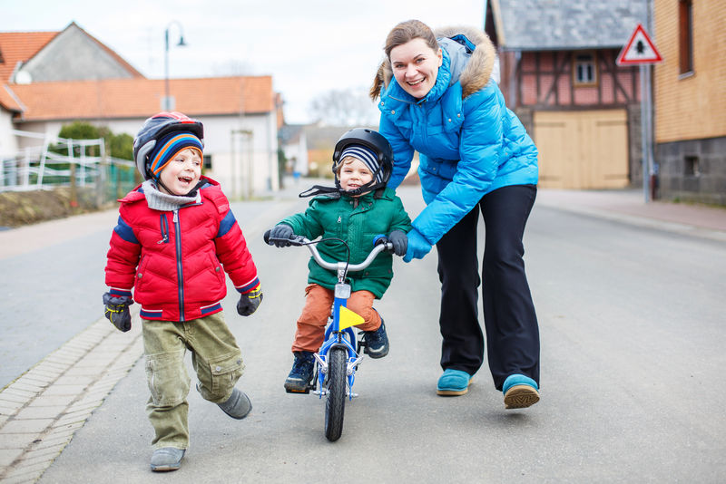 年轻的母亲教她两岁的小儿子骑自行车