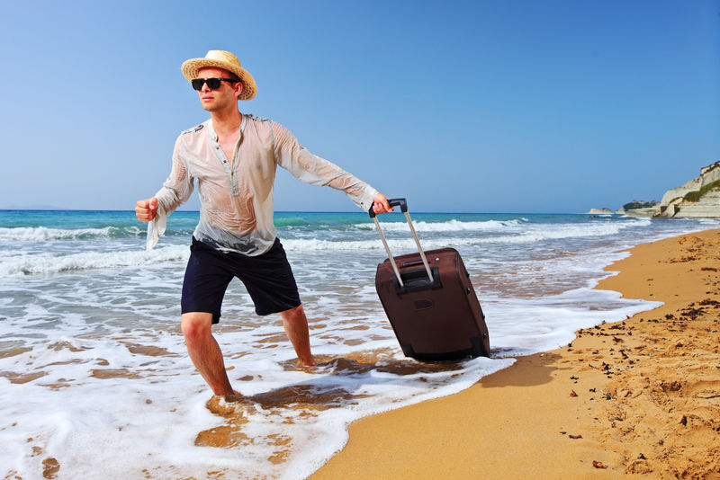 一个游客在科孚岛的海滩上提着一个手提箱