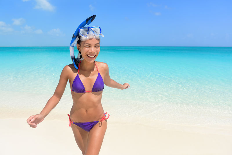 海滩度假-亚洲女子游泳乐趣美丽性感的年轻女性成年人带着潜水面罩穿着紫色比基尼在她的旅游假期里从水里跑出来