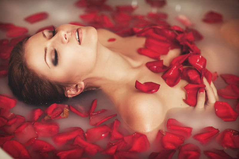 在浴缸里有牛奶和玫瑰花瓣的迷人女孩-嫩肤嫩肤水疗-SPA沙龙性感化妆女-漂亮性感的深色带红色花瓣的按摩浴缸放松