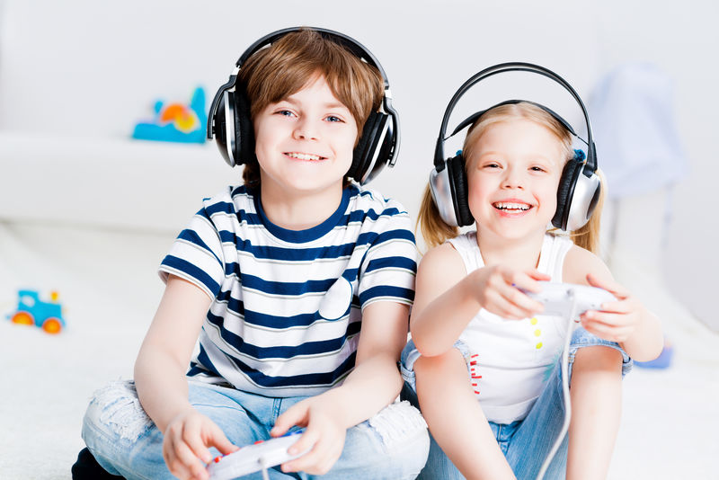 可爱的男孩和女孩坐在地板上用无线耳机玩游戏机