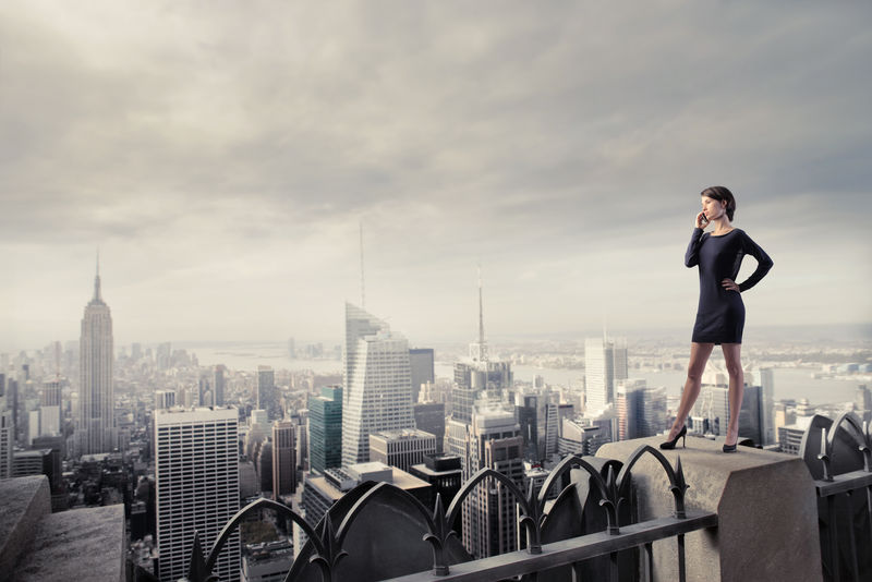漂亮的女商人站在摩天大楼的屋顶在一个城市