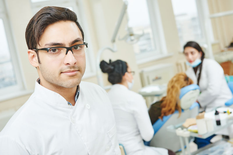 亚洲男性牙医坐在诊所时穿着实验服的照片