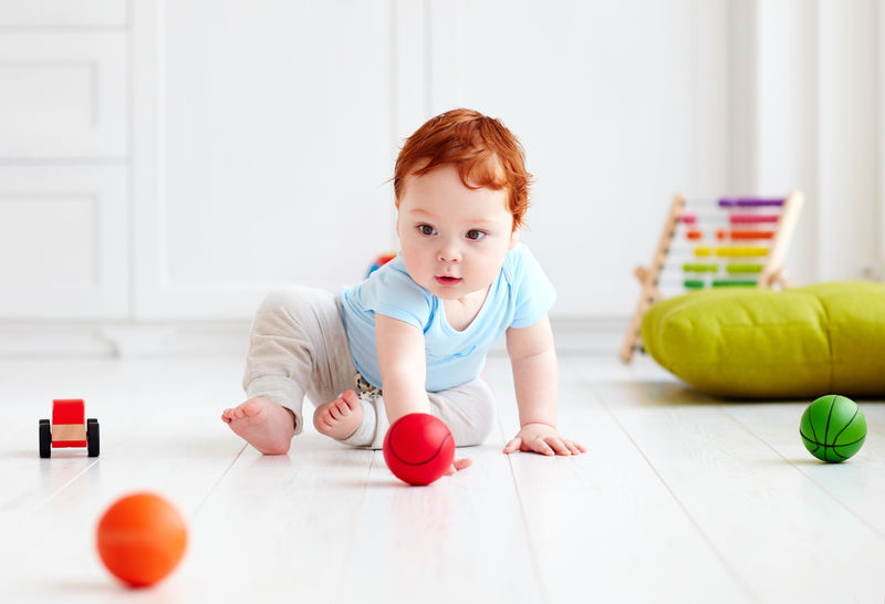 可爱的婴儿宝宝在家里爬在地板上，玩着五颜六色的球。