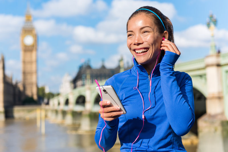 伦敦跑步生活方式女性在智能手机上收听健身音乐播放列表。在城市街道参加跑步训练的女性。英国伦敦威斯敏斯特桥大本附近的跑步女孩