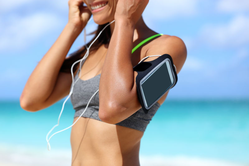 健身手机臂章跑步女子戴耳机。运动智能手机外壳的支架触摸屏带人穿在海滩跑步锻炼锻炼耳机女臂特写。