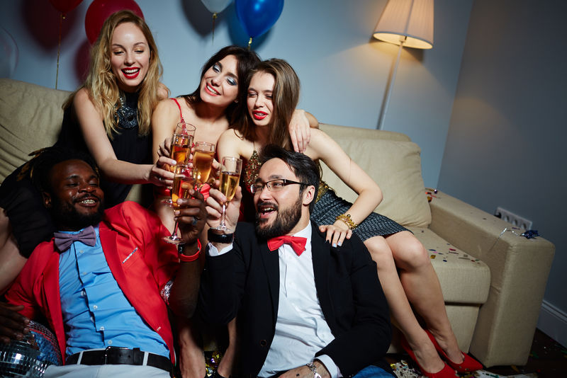 多的男女朋友坐在沙发上和地板上，在庆祝新年的时候碰着香槟长笛。