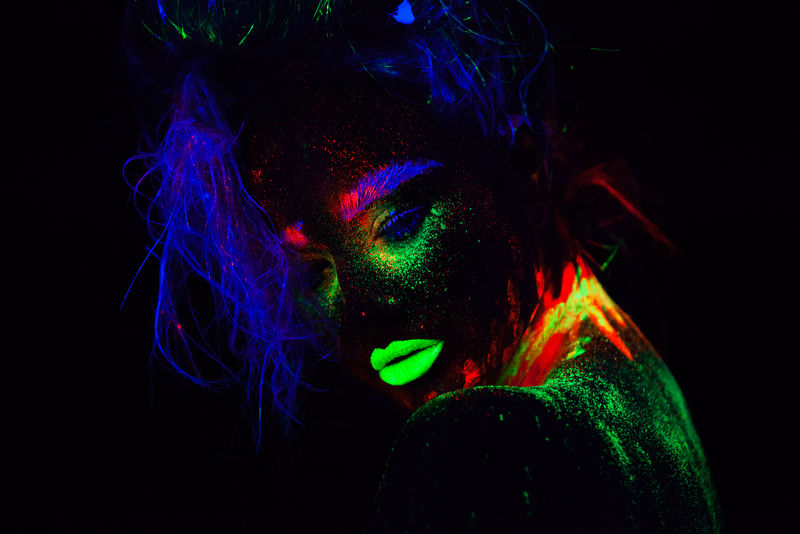 美丽的外星模特，蓝色头发，绿色嘴唇，霓虹灯下。它是一幅荧光彩妆的美丽模特的近照，是一幅彩色的女性在紫外光下摆姿势的艺术设计。