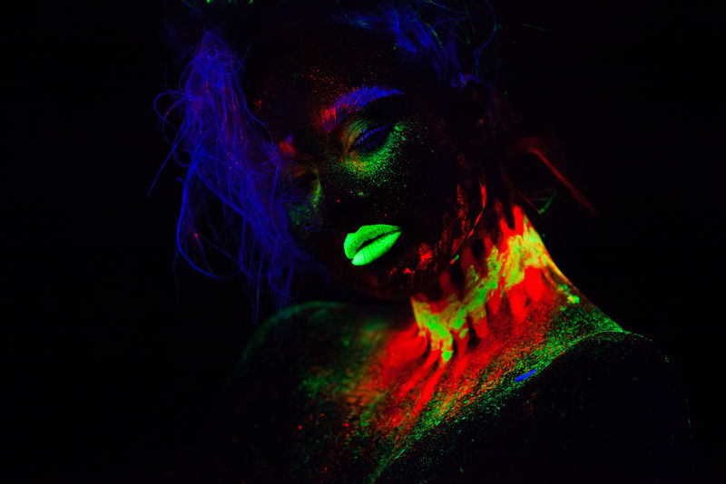 美丽的外星模特，蓝色头发，绿色嘴唇，霓虹灯下。这是一幅荧光彩妆的美丽模特肖像，彩妆的女性在紫外光下摆姿势的艺术设计。