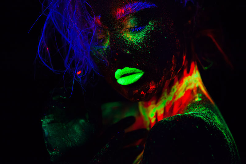 美丽的外星模特，蓝色头发，绿色嘴唇，霓虹灯下。它是一幅荧光彩妆的美丽模特的近照，是一幅彩色的女性在紫外光下摆姿势的艺术设计。
