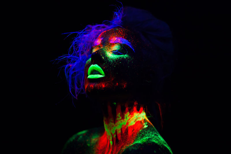 美丽的外星模特，蓝色头发，绿色嘴唇，霓虹灯下。这是一幅荧光彩妆的美丽模特肖像，彩妆的女性在紫外光下摆姿势的艺术设计。