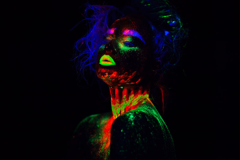美丽的外星模特，有着蓝色的空气和霓虹灯下的绿色嘴唇。这是一幅荧光彩妆的美丽模特肖像，彩妆的女性在紫外光下摆姿势的艺术设计。